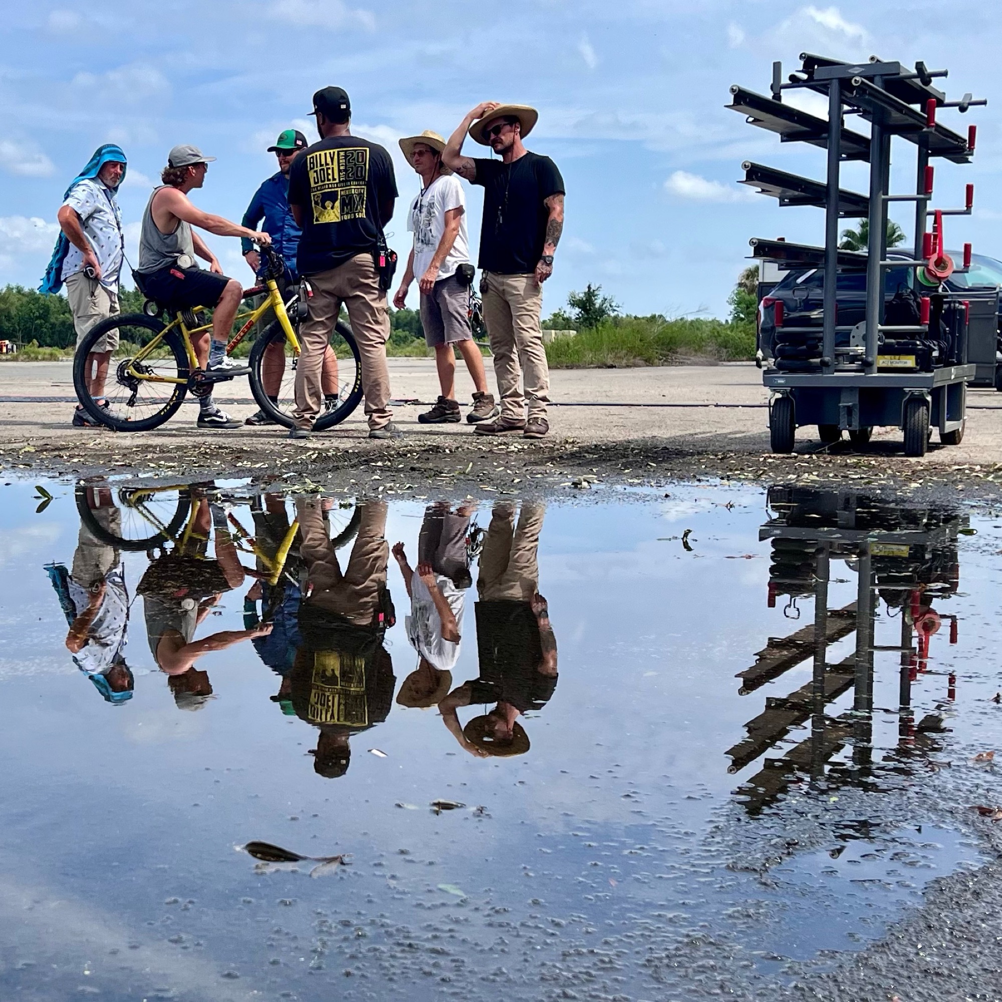 Film crew and grip cart reflected in a puddle on location
